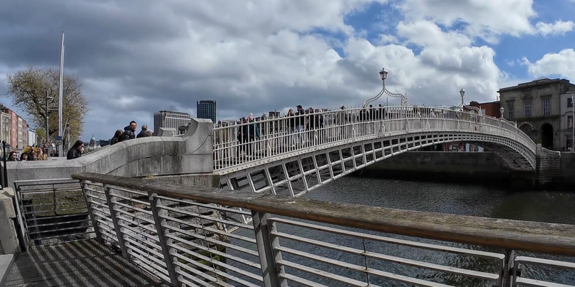 Ha'penny Bridge, Dublino. Il celebre Ha'penny Bridge attraversa il fiume Liffey in una rara giornata di sole nel cuore di Dublino. Simbolo storico della capitale irlandese, il ponte rappresenta ancora oggi uno dei luoghi più iconici della città, meta quotidiana di residenti, lavoratori e turisti.