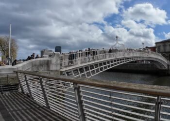 Ha'penny Bridge, Dublino. Il celebre Ha'penny Bridge attraversa il fiume Liffey in una rara giornata di sole nel cuore di Dublino. Simbolo storico della capitale irlandese, il ponte rappresenta ancora oggi uno dei luoghi più iconici della città, meta quotidiana di residenti, lavoratori e turisti.