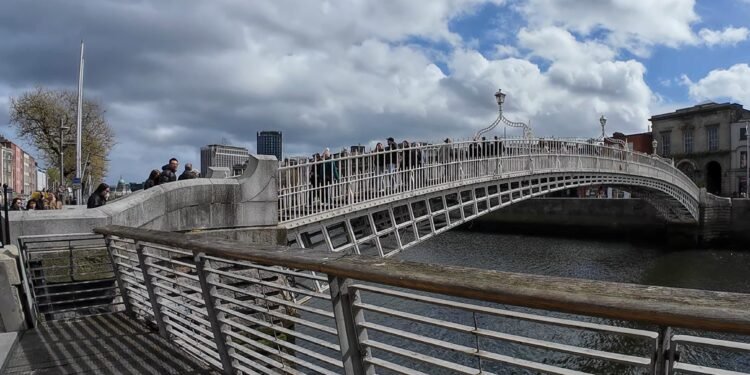 Ha'penny Bridge, Dublino. Il celebre Ha'penny Bridge attraversa il fiume Liffey in una rara giornata di sole nel cuore di Dublino. Simbolo storico della capitale irlandese, il ponte rappresenta ancora oggi uno dei luoghi più iconici della città, meta quotidiana di residenti, lavoratori e turisti.
