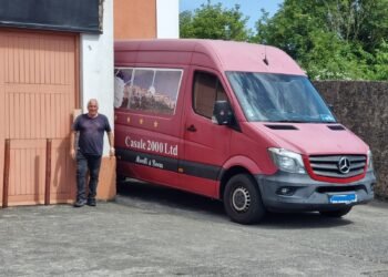 Francesco Morelli accanto al suo inconfondibile Mercedes Sprinter rosso, personalizzato con immagini panoramiche di Casalattico e Cashel, simbolo del lungo viaggio che collega l'Italia all'Irlanda.