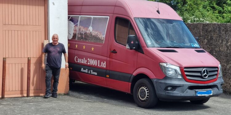 Francesco Morelli accanto al suo inconfondibile Mercedes Sprinter rosso, personalizzato con immagini panoramiche di Casalattico e Cashel, simbolo del lungo viaggio che collega l'Italia all'Irlanda.