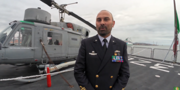 Alessandro De Lucia, comandante di Nave Etna, sul ponte di volo dell’unità della Marina Militare Italiana, con alle spalle l’elicottero di bordo.