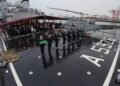 Sul ponte di volo di ITS ETNA, i militari della Marina Militare Italiana schierati con il Tricolore solennemente ripiegato al termine dell’Ammaina Bandiera. A destra l’elicottero di bordo, mentre sullo sfondo gli ospiti – rappresentanti istituzionali, diplomatici, esponenti del mondo politico e imprenditoriale e membri della comunità – osservano con attenzione uno dei momenti più suggestivi della serata a Dublin Port.