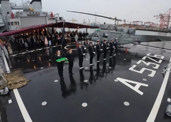 Sul ponte di volo di ITS ETNA, i militari della Marina Militare Italiana schierati con il Tricolore solennemente ripiegato al termine dell’Ammaina Bandiera. A destra l’elicottero di bordo, mentre sullo sfondo gli ospiti – rappresentanti istituzionali, diplomatici, esponenti del mondo politico e imprenditoriale e membri della comunità – osservano con attenzione uno dei momenti più suggestivi della serata a Dublin Port.