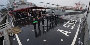 Sul ponte di volo di ITS ETNA, i militari della Marina Militare Italiana schierati con il Tricolore solennemente ripiegato al termine dell’Ammaina Bandiera. A destra l’elicottero di bordo, mentre sullo sfondo gli ospiti – rappresentanti istituzionali, diplomatici, esponenti del mondo politico e imprenditoriale e membri della comunità – osservano con attenzione uno dei momenti più suggestivi della serata a Dublin Port.
